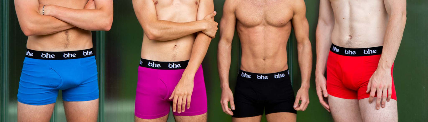 The lower half of 4 men wearing blue, purple/magenta, black and red boxer shorts with black waist band containing repeated white 'ohe logo